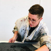 Aster (white person with short brown hair) screen-printing a t-shirt